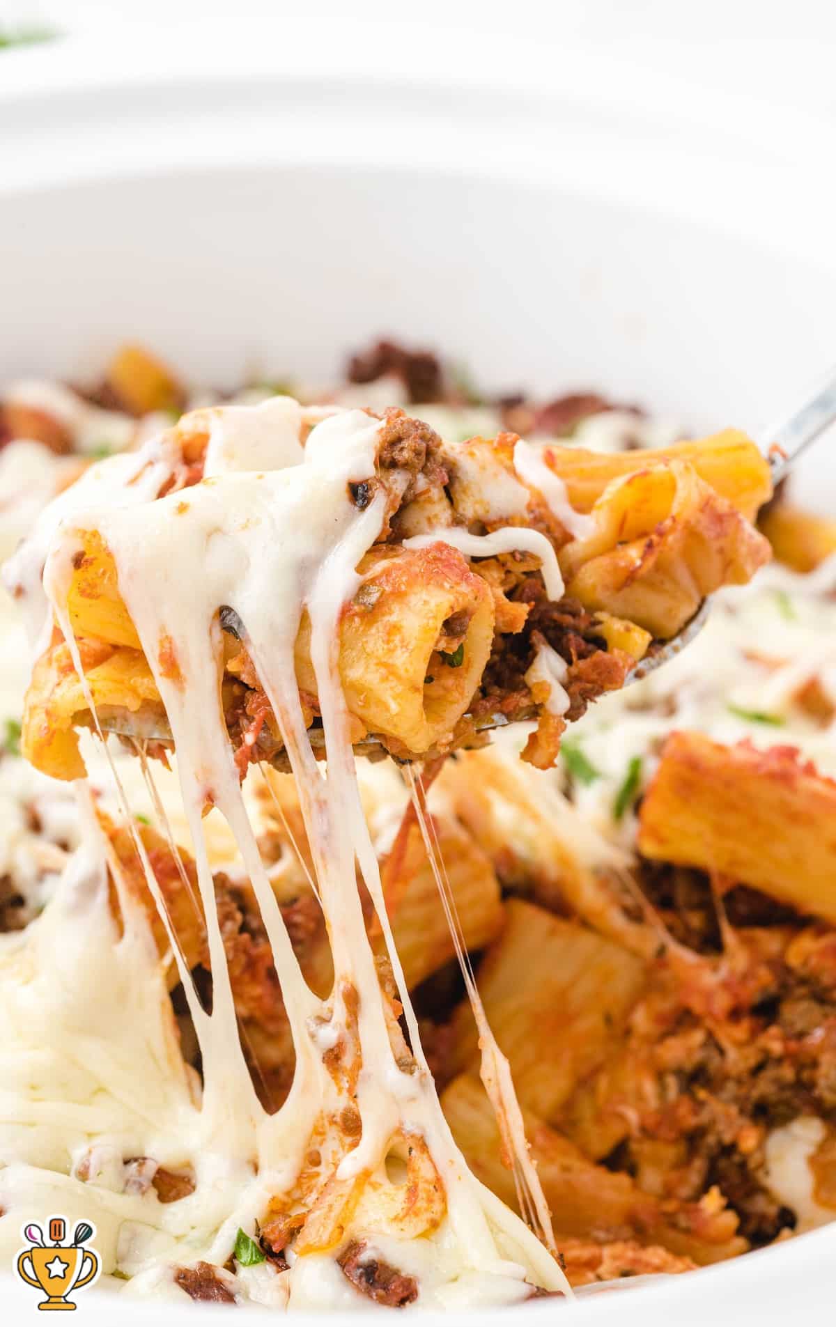 Mouthwatering serving of baked ziti being lifted with a spoon from the crockpot, with cheese stretching and melted over noodles.