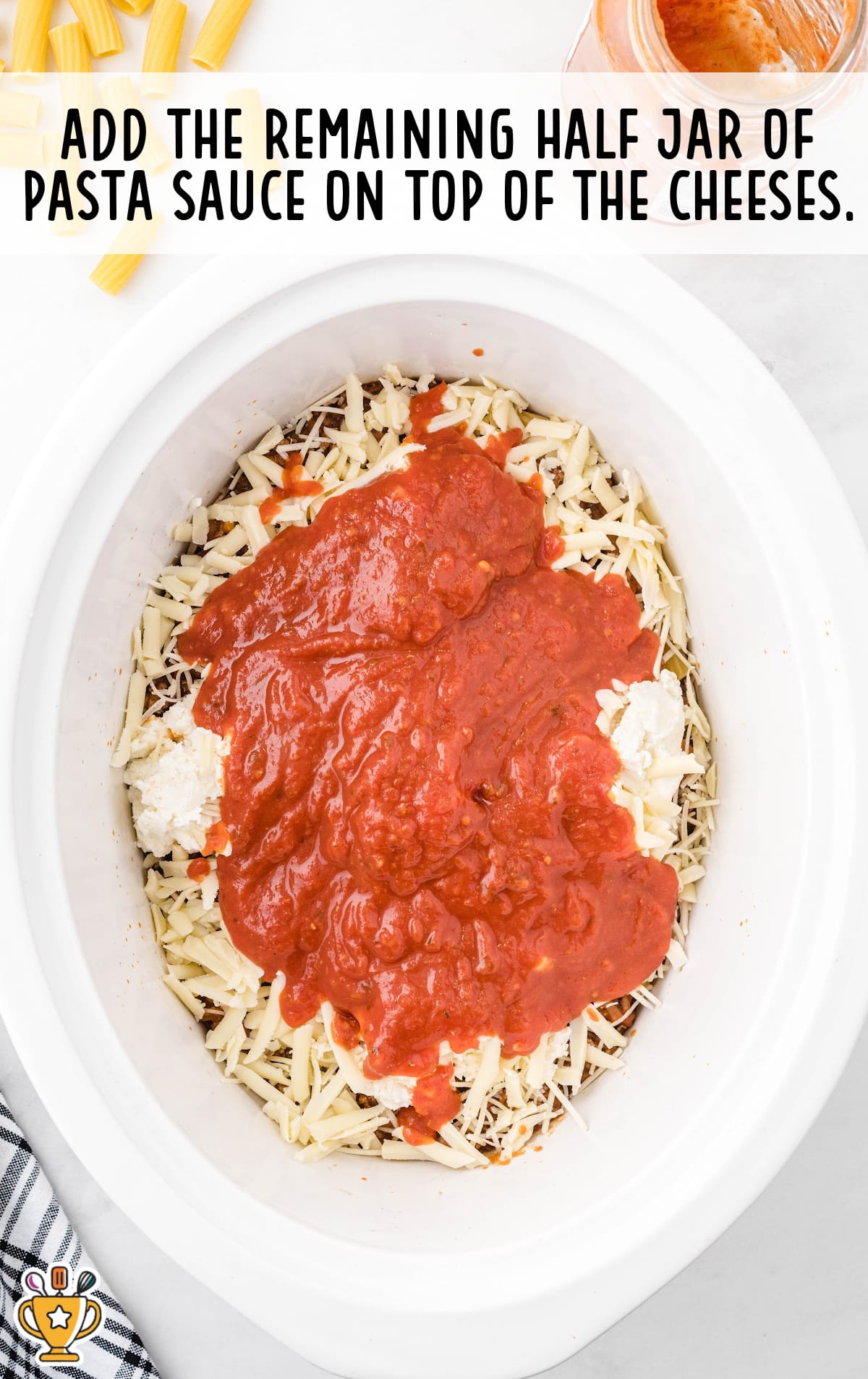 Top view of a white crockpot filled with shredded cheese and ricotta, topped with a layer of red pasta sauce.