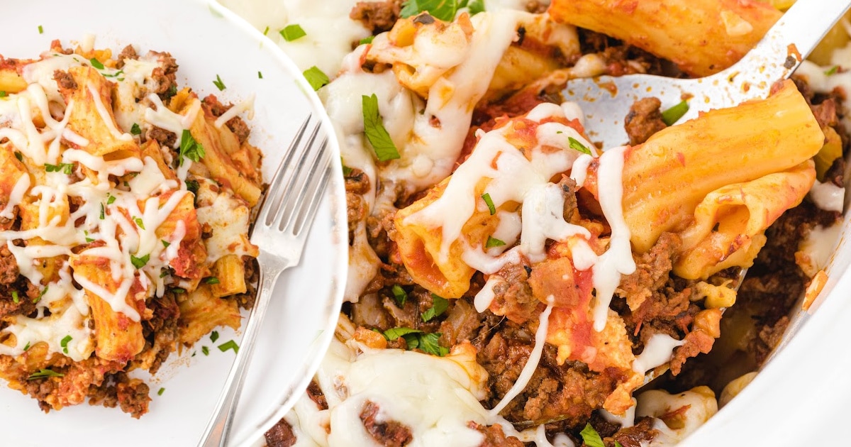 Overhead photo showing a white plate of baked ziti next to a crockpot, both filled with pasta, meat, cheese, and herbs.