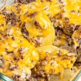 A glass baking dish filled with hamburger potato casserole topped with golden melted cheese and ground beef.