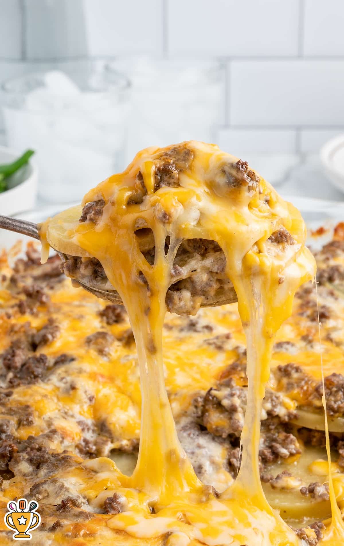 Spoonful of cheesy hamburger potato casserole being lifted, showing gooey melted cheese stretching with beef and potatoes.