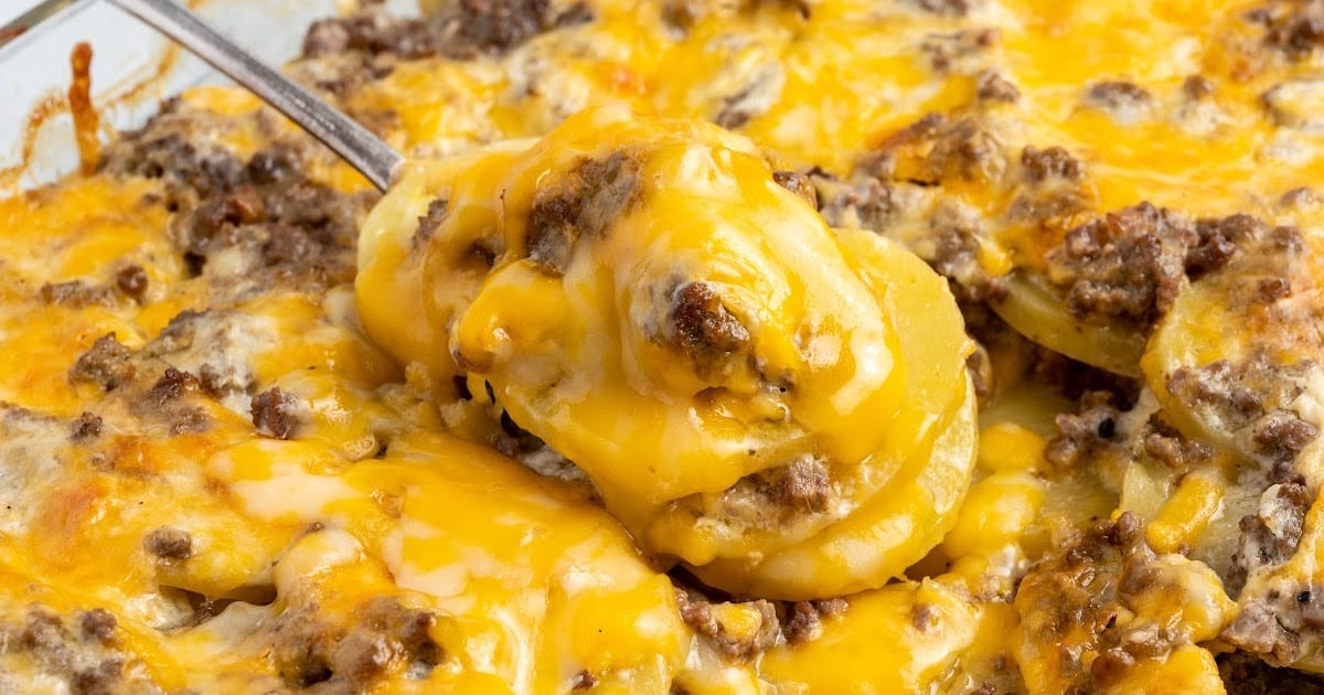 Spoonful of cheesy hamburger potato casserole lifted from the dish, showing layers of potatoes, beef, and gooey melted cheese.