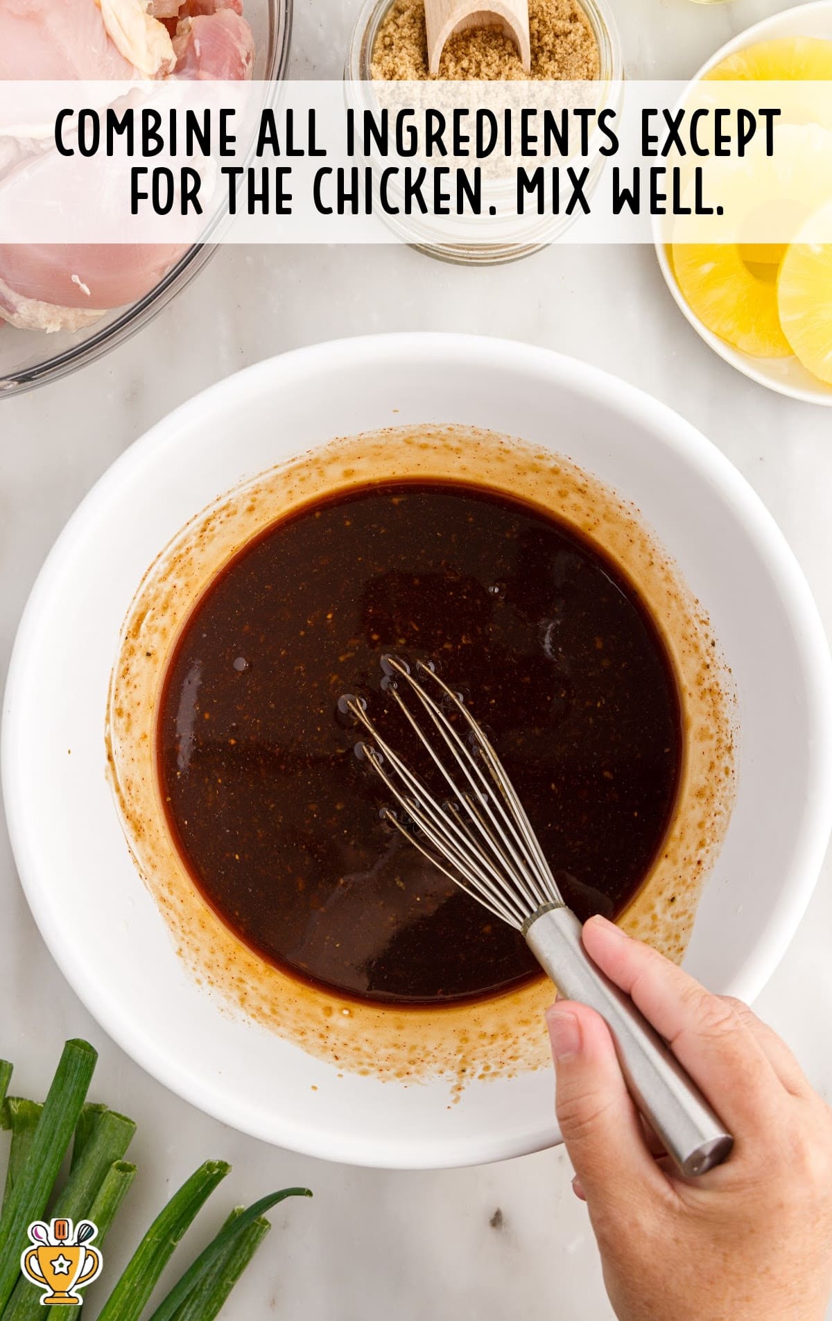 Hand whisking a dark pineapple-soy marinade in a white bowl with other ingredients visible around the counter.