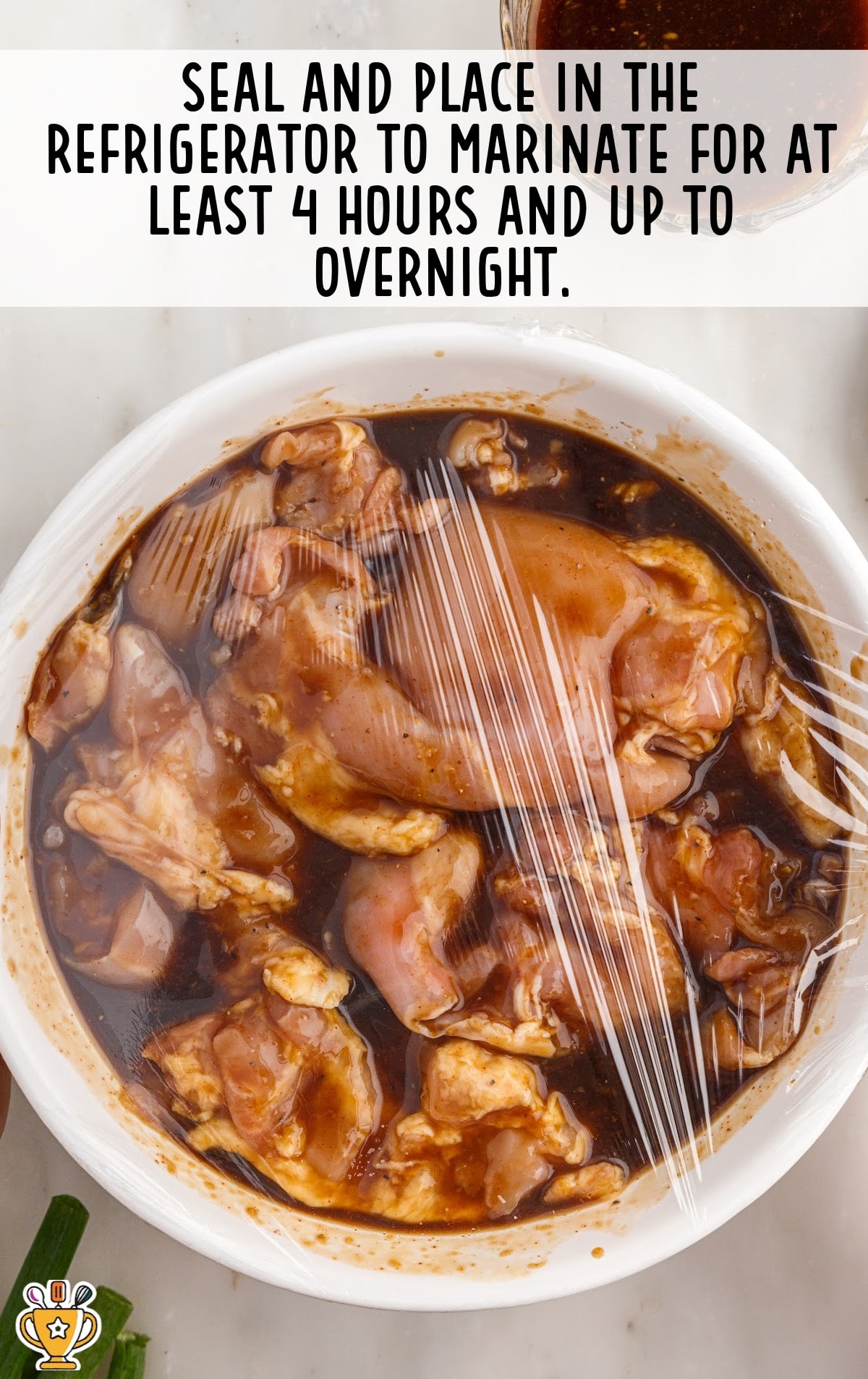 Raw chicken pieces covered in dark marinade, sealed with plastic wrap, ready to refrigerate.