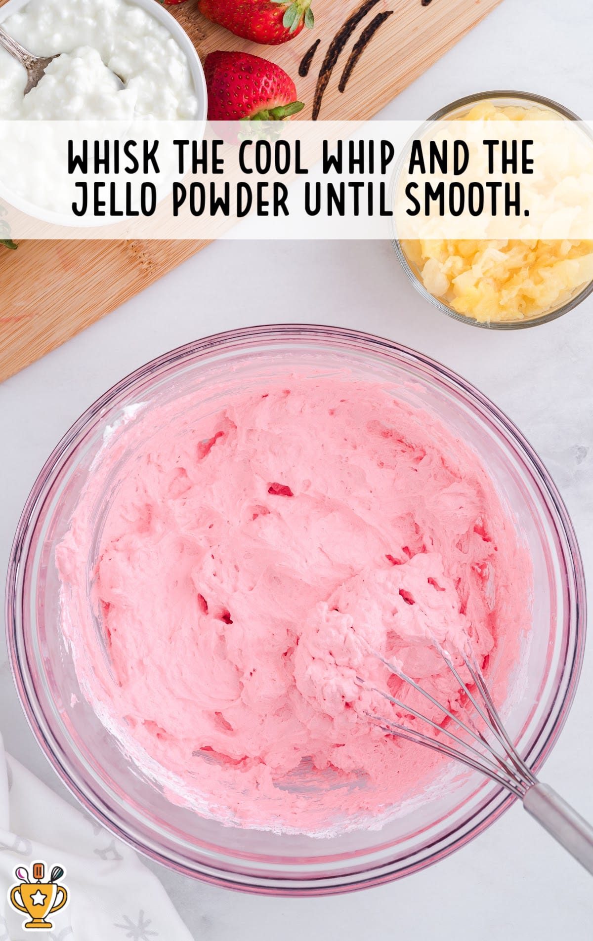 Instructional image showing a glass bowl of pink whipped mixture being whisked. Caption reads: &ldquo;Whisk the Cool Whip and the Jello powder until smooth.&rdquo;