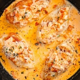 Four golden chicken breasts simmering in a creamy tomato Parmesan sauce inside a cast iron skillet, ready to serve.