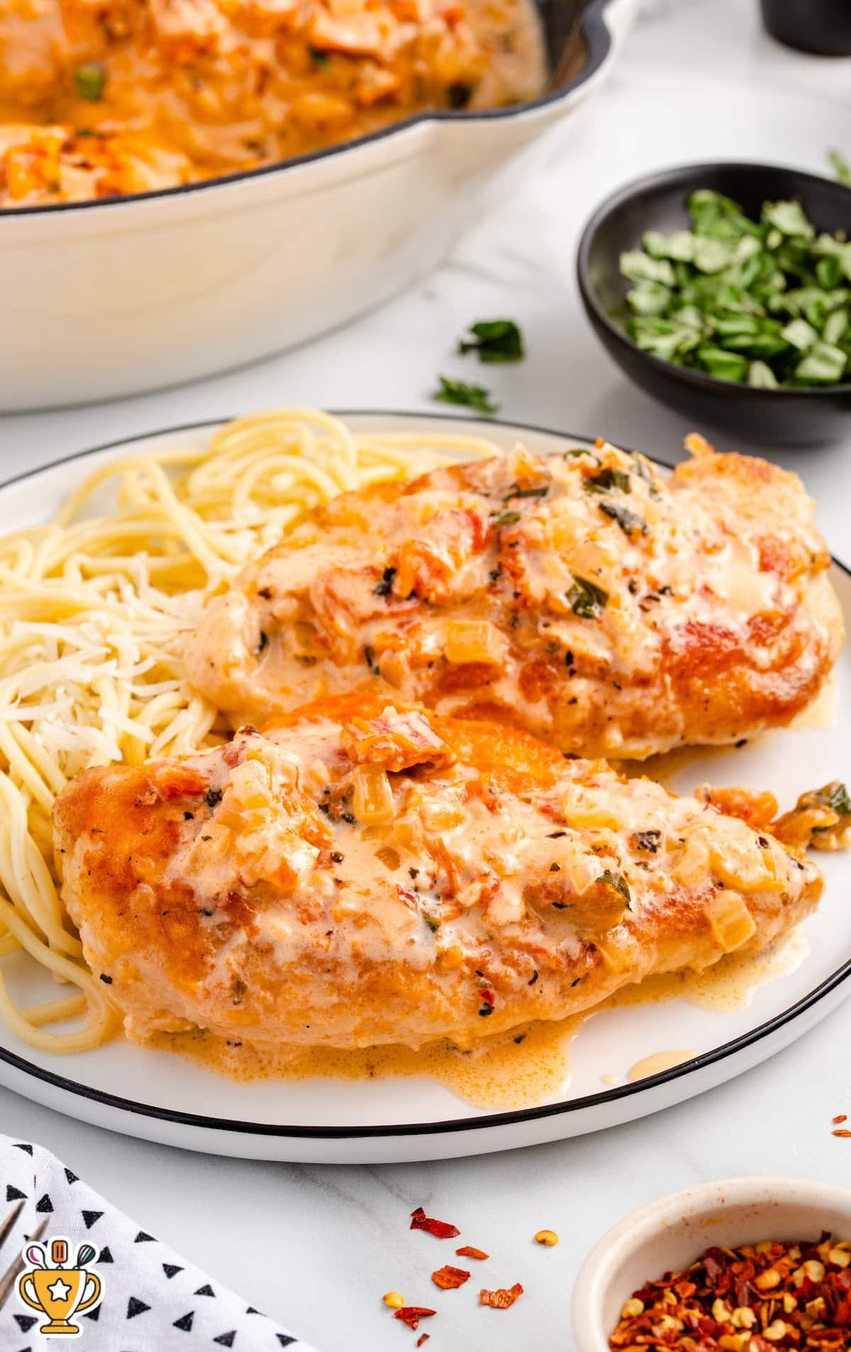 Plate of creamy Marry Me Chicken with spaghetti, topped with rich sauce and herbs, with a skillet in the background.