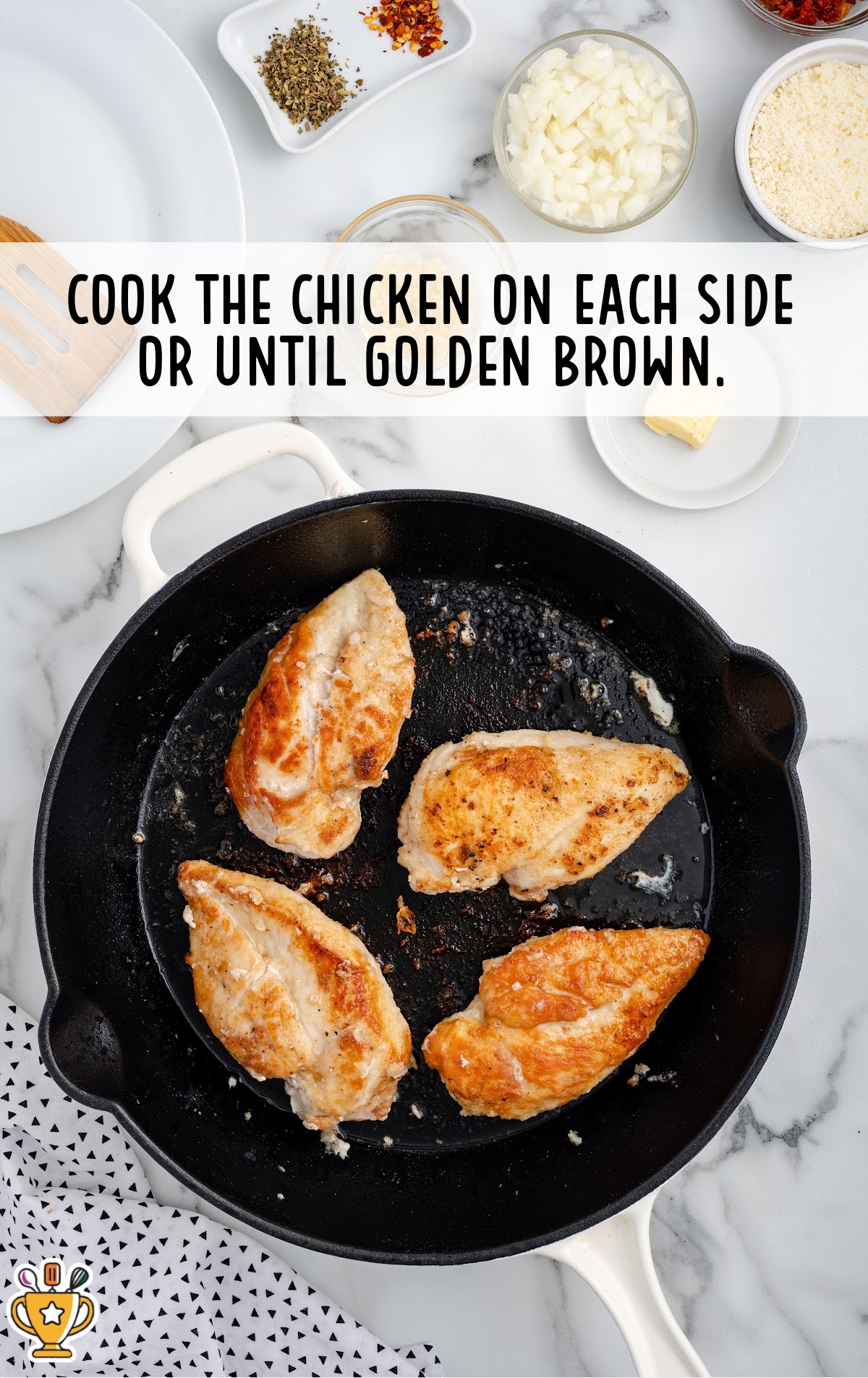 Four chicken breasts cooking in a black skillet until golden brown, with ingredient bowls in the background.