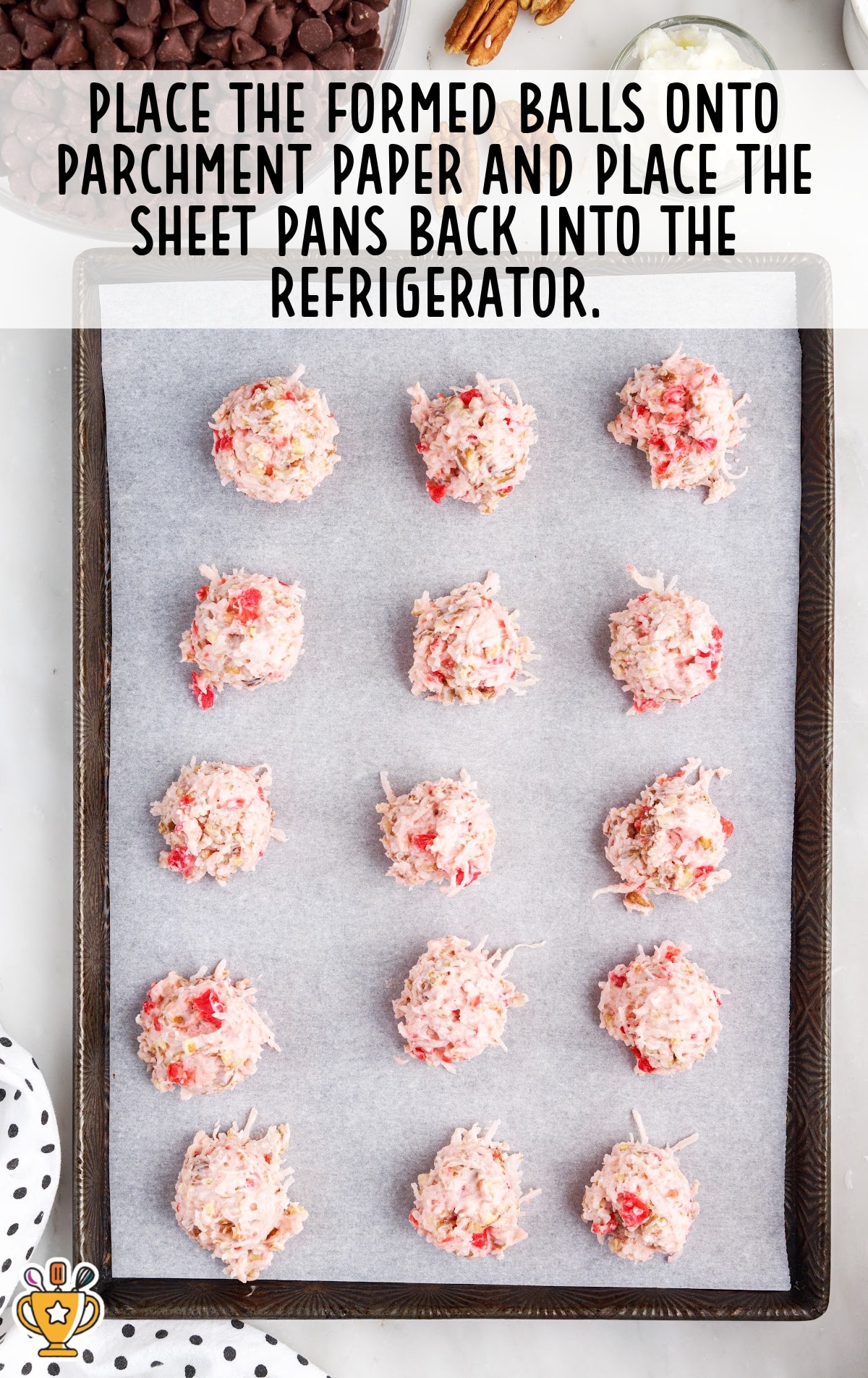 Twelve coconut-cherry-pecan filling balls arranged neatly on a parchment-lined baking sheet, ready to be chilled in the fridge.