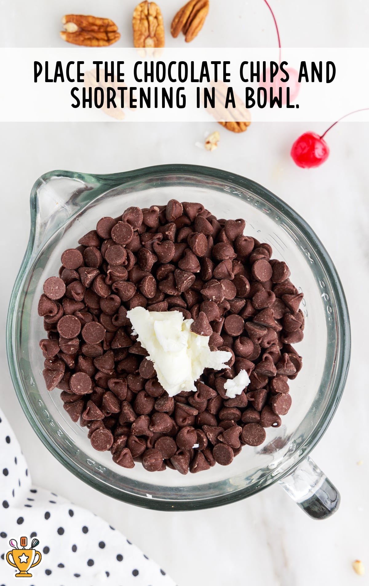 Glass bowl filled with chocolate chips and a scoop of white shortening, ready for melting on a marble countertop.
