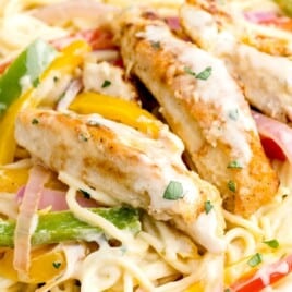 Brightly lit plate of creamy Olive garden chicken scampi pasta with seared chicken strips, red onion, and mixed bell peppers.