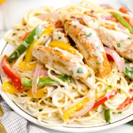 Plate of chicken scampi with spaghetti, sautéed bell peppers, and creamy garlic parmesan sauce, garnished with fresh parsley.