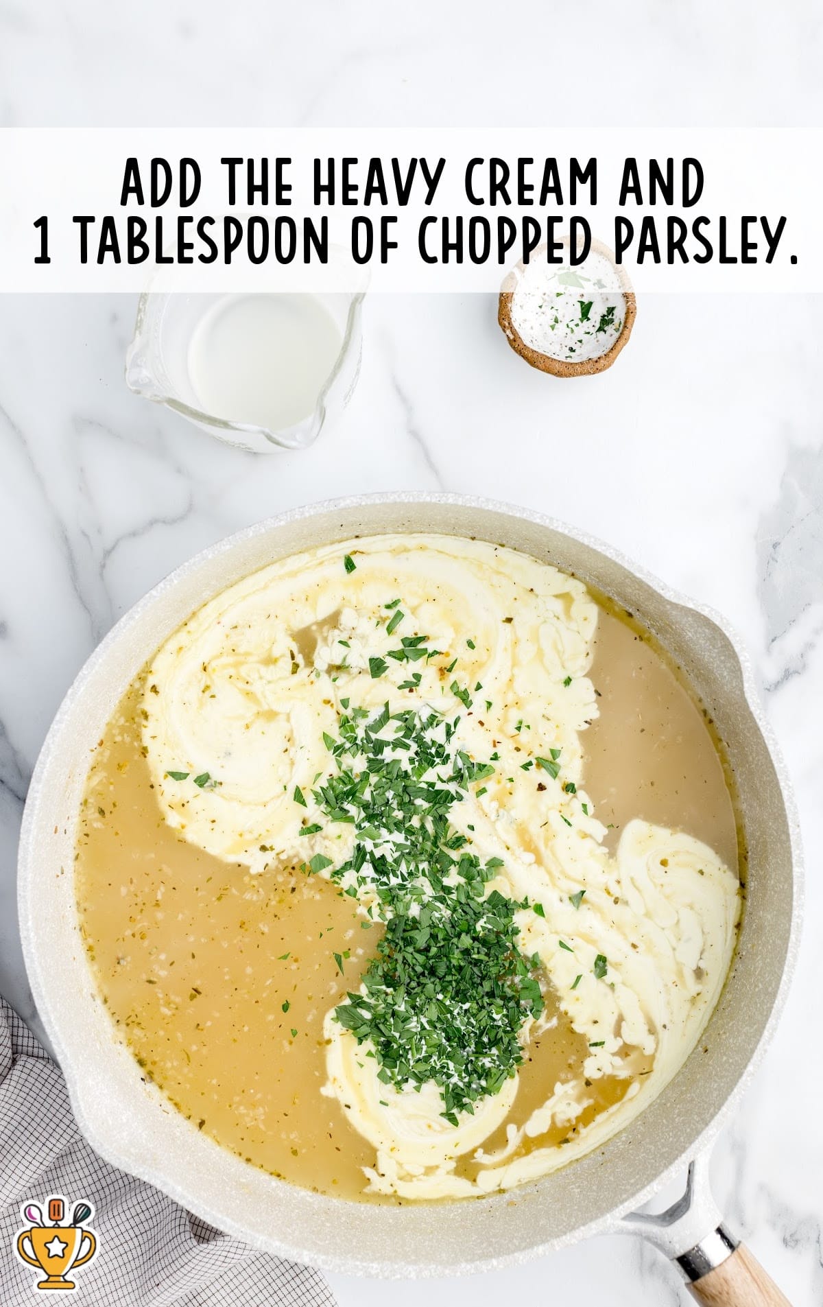 Creamy sauce in a skillet made with chicken broth and heavy cream, topped with freshly chopped parsley before stirring.