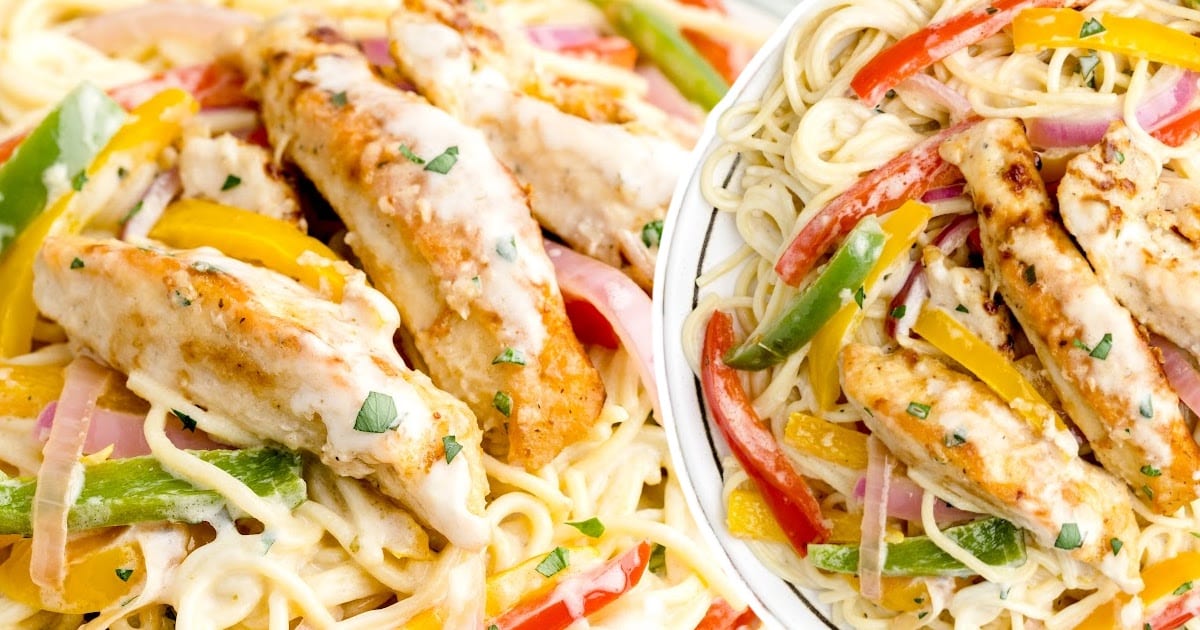 Extreme close-up of tender chicken strips on a bed of spaghetti with sliced red onions and colorful bell peppers in garlic cream sauce.
