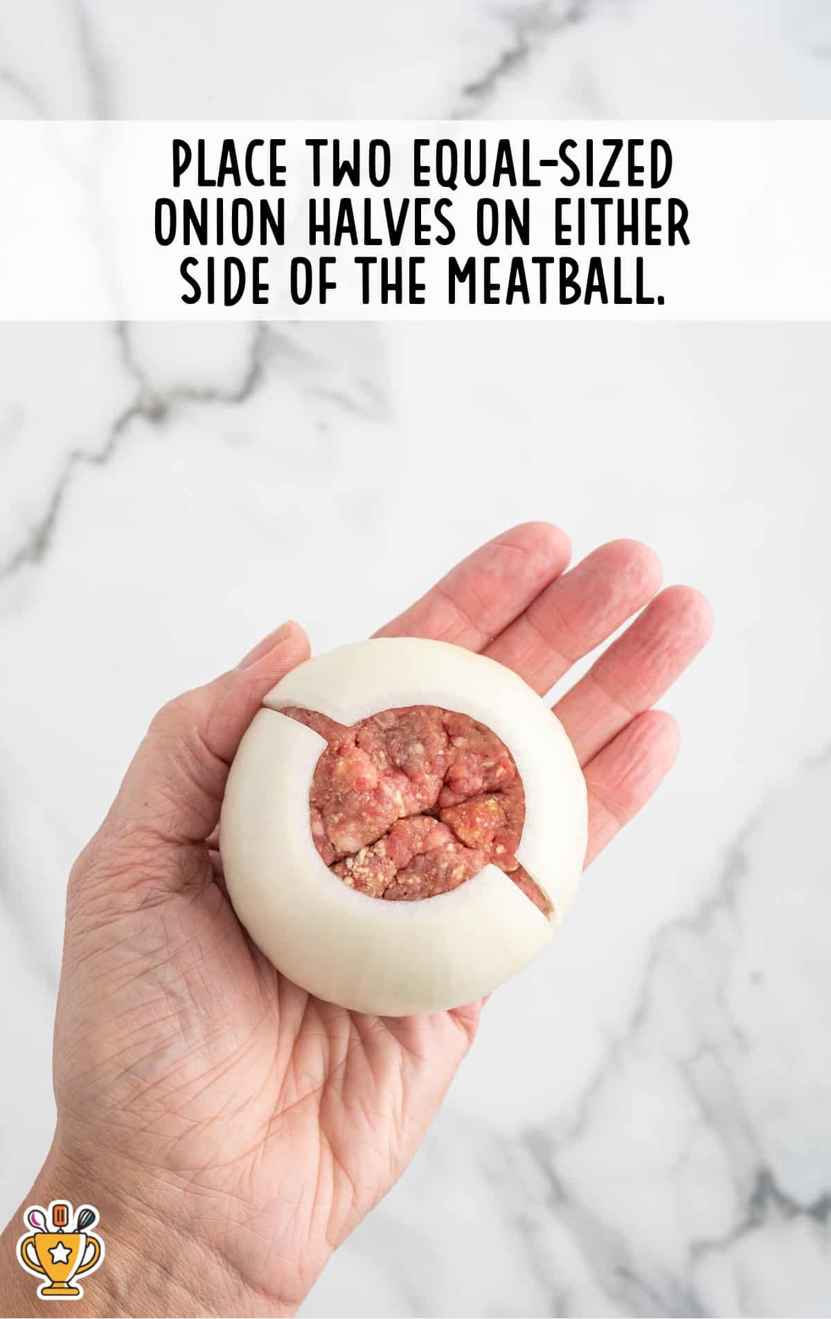 A hand holds a raw onion filled with ground beef, showing how two onion halves encase a meatball in the center.