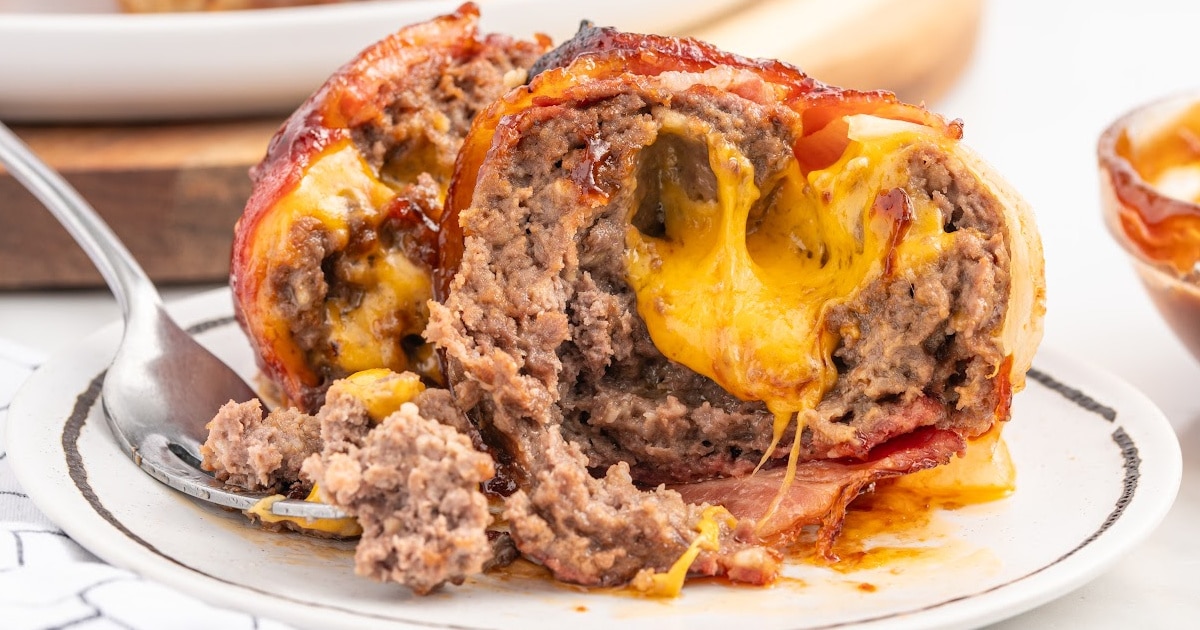 A cheesy onion bomb cut in half, revealing a gooey melted cheddar center surrounded by juicy ground beef and crispy bacon.