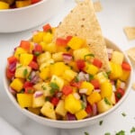 Close-up of vibrant pineapple mango salsa in a white bowl, garnished with cilantro and served with a tortilla chip.