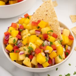 Close-up of vibrant pineapple mango salsa in a white bowl, garnished with cilantro and served with a tortilla chip.