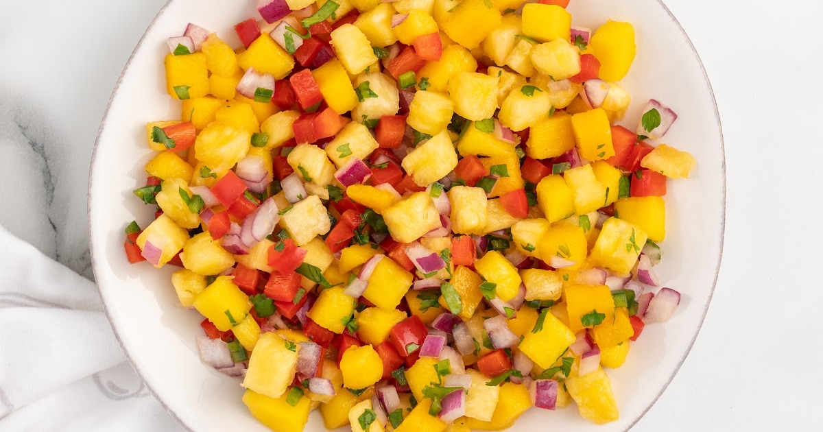 Overhead view of pineapple mango salsa in a round white bowl, highlighting the bright colors of the diced ingredients on a light background.