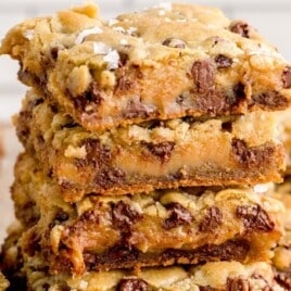 A close-up of a stack of salted caramel chocolate chip cookie bars, baked golden brown with melted chocolate and gooey caramel centers.