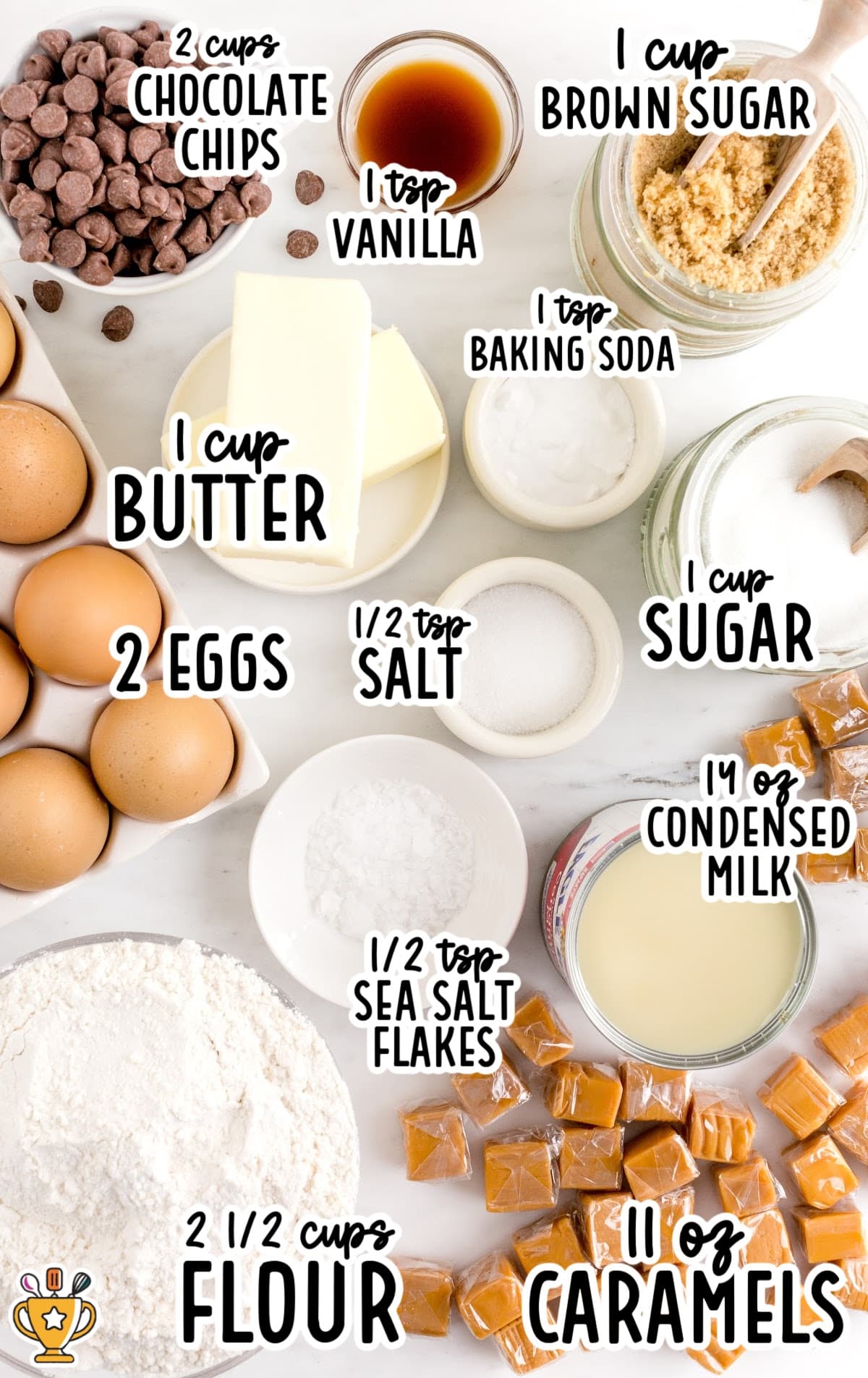 Flat lay of ingredients for salted caramel chocolate chip cookie bars, including butter, eggs, flour, sugars, chocolate chips, caramels, condensed milk, vanilla, salt, and baking soda.