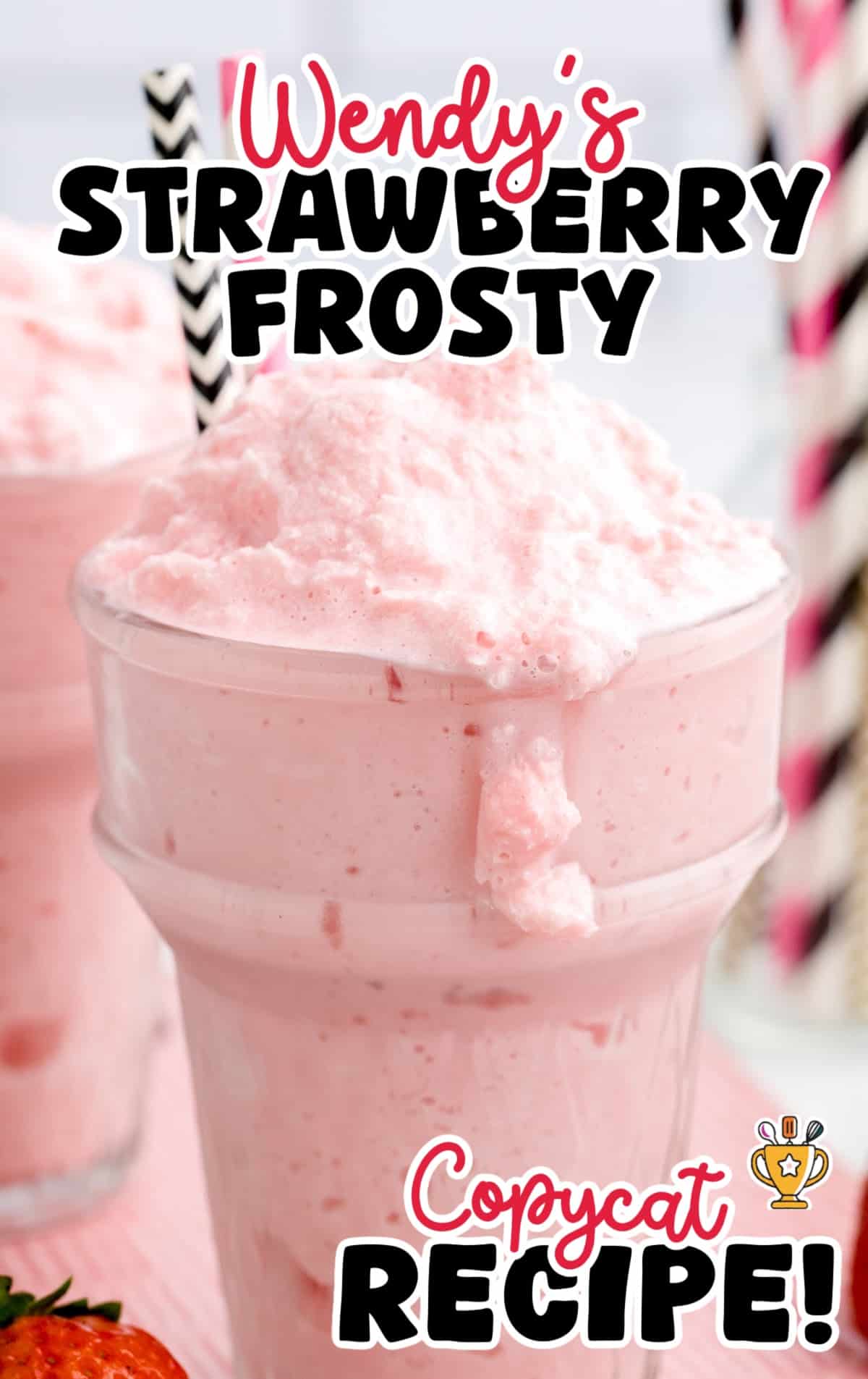 Wendy&rsquo;s copycat strawberry frosty in a tall glass, overflowing with pink frothy texture, with bold recipe text and a striped straw on top.