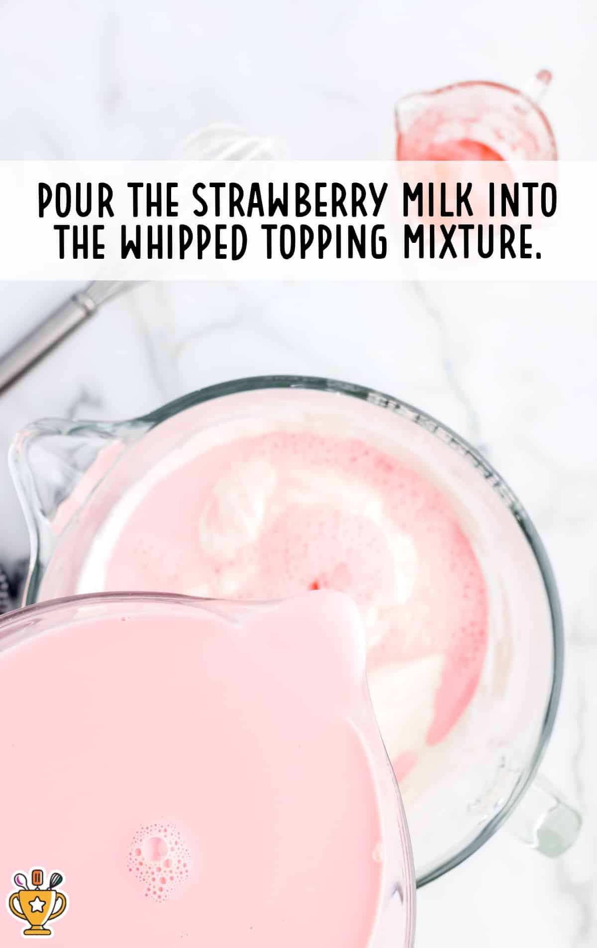 A glass measuring cup pouring strawberry milk mixture into a large mixing bowl with whipped topping, with overlay text &ldquo;Pour the strawberry milk into the whipped topping mixture.&rdquo;