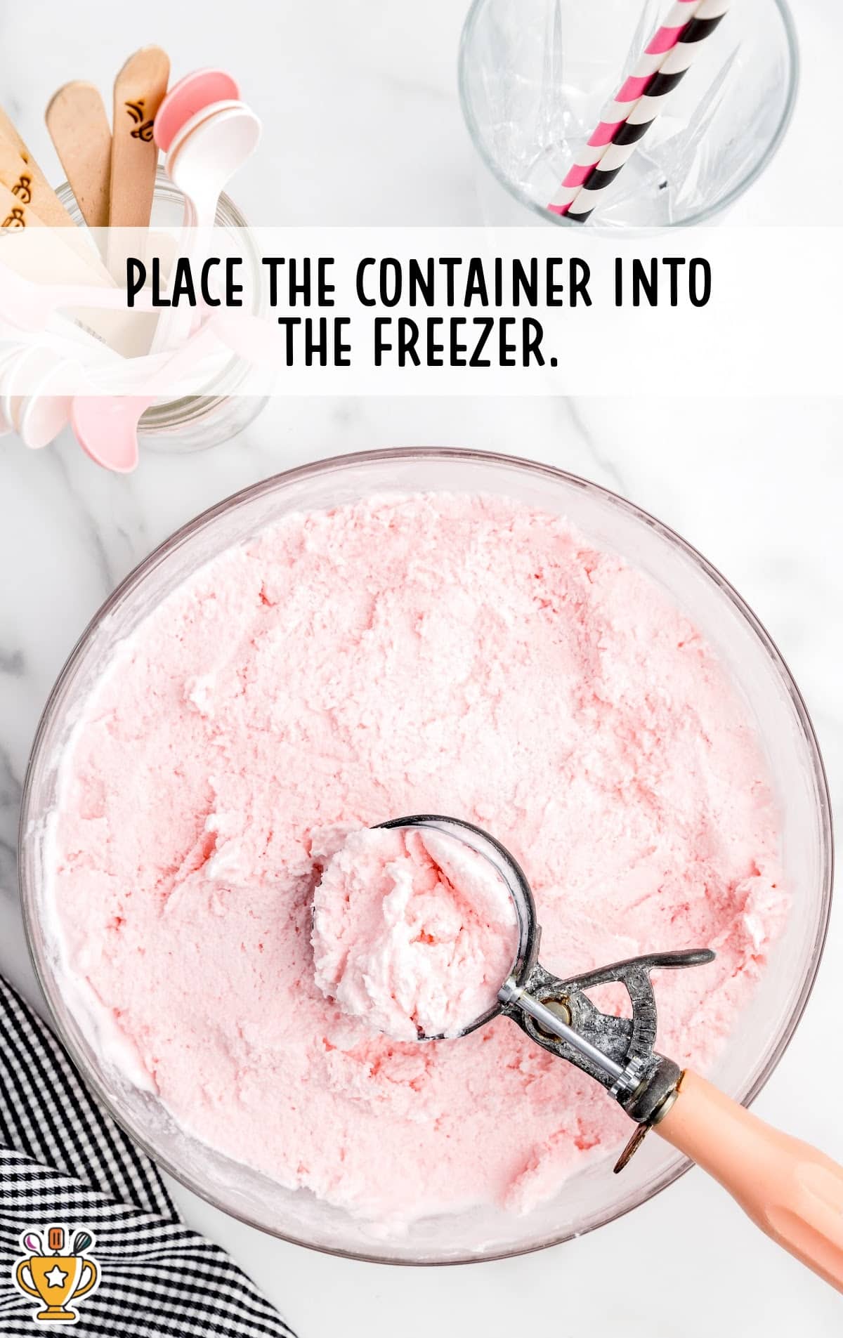 A large bowl filled with frozen pink strawberry frosty being scooped with an ice cream scooper, with overlay text &ldquo;Place the container into the freezer.&rdquo;