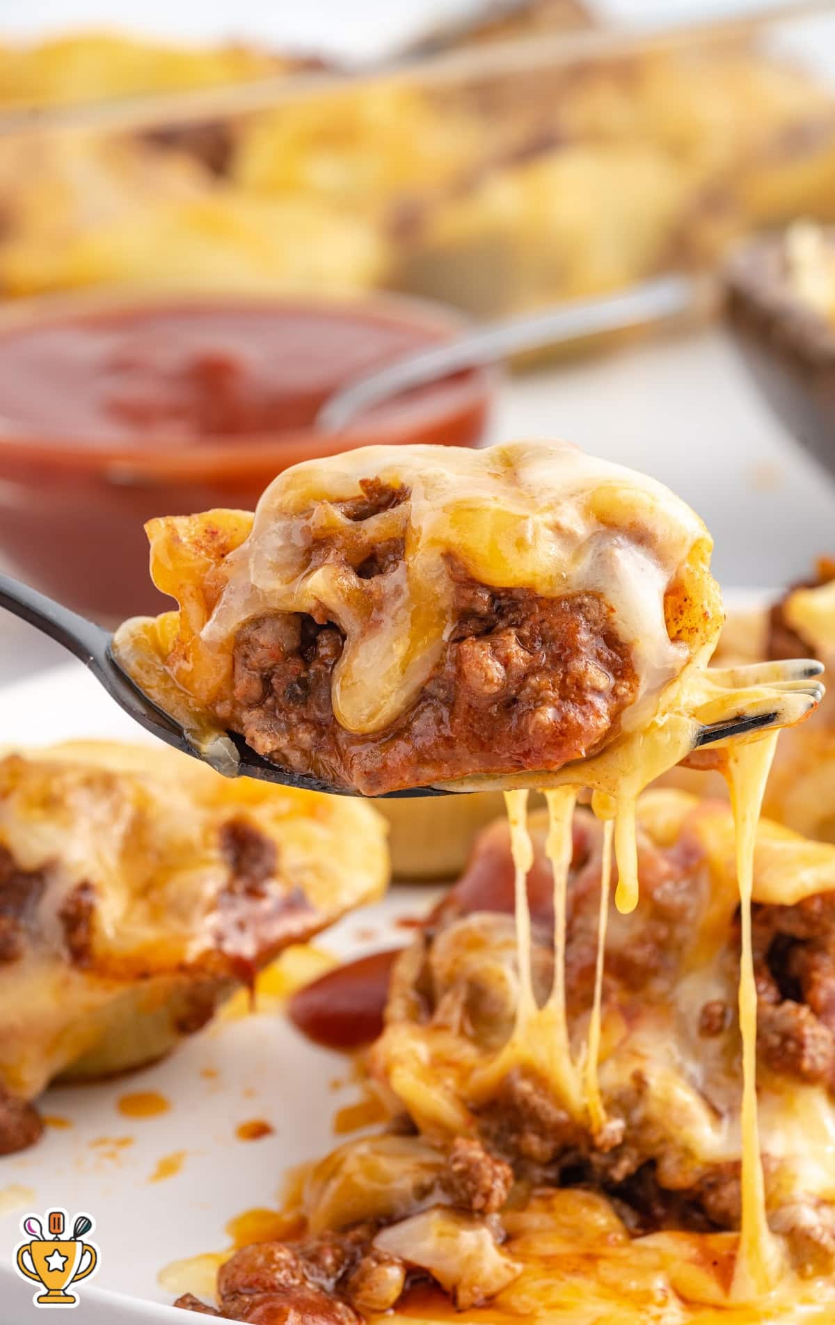 Cheesy stuffed shell filled with seasoned ground beef and taco sauce being lifted from a plate, with melted cheese dripping down.