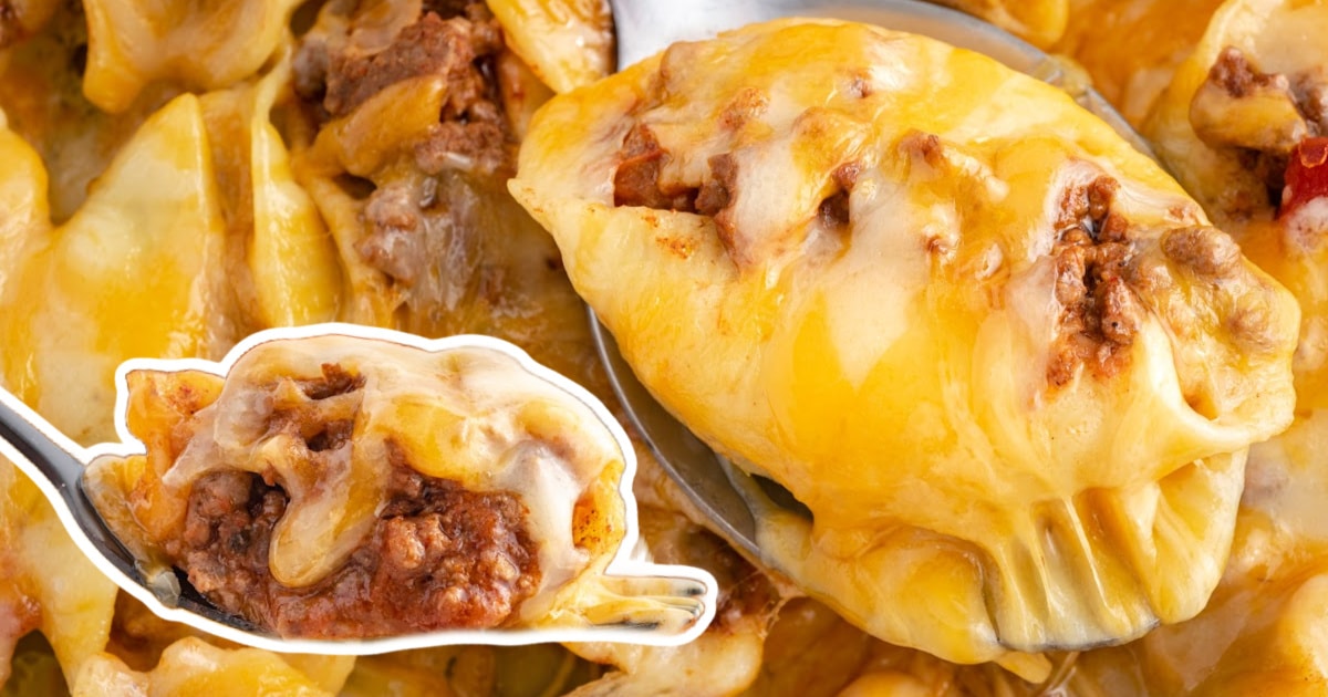 A spoonful of cheesy taco stuffed shell highlighted over a close-up of a full baking dish with shells baked to golden perfection.