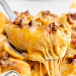 Bright and colorful image of a taco stuffed shell lifted above a casserole dish, with stretchy melted cheese and overlay text highlighting how easy and cheesy the recipe is.