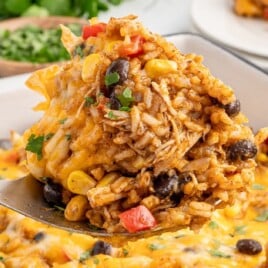 Cheesy Mexican chicken and rice casserole with black beans, corn, and peppers being served from baking dish, family-friendly dinner idea.