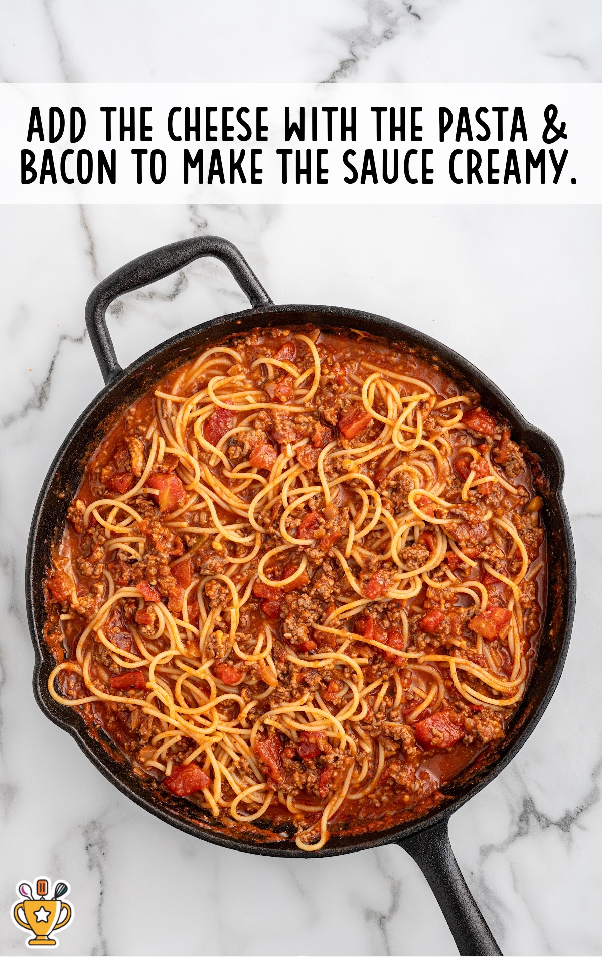 Overhead shot of a cast iron skillet filled with cowboy spaghetti, with overlay tip: &ldquo;Add the cheese with the pasta & bacon.&rdquo;