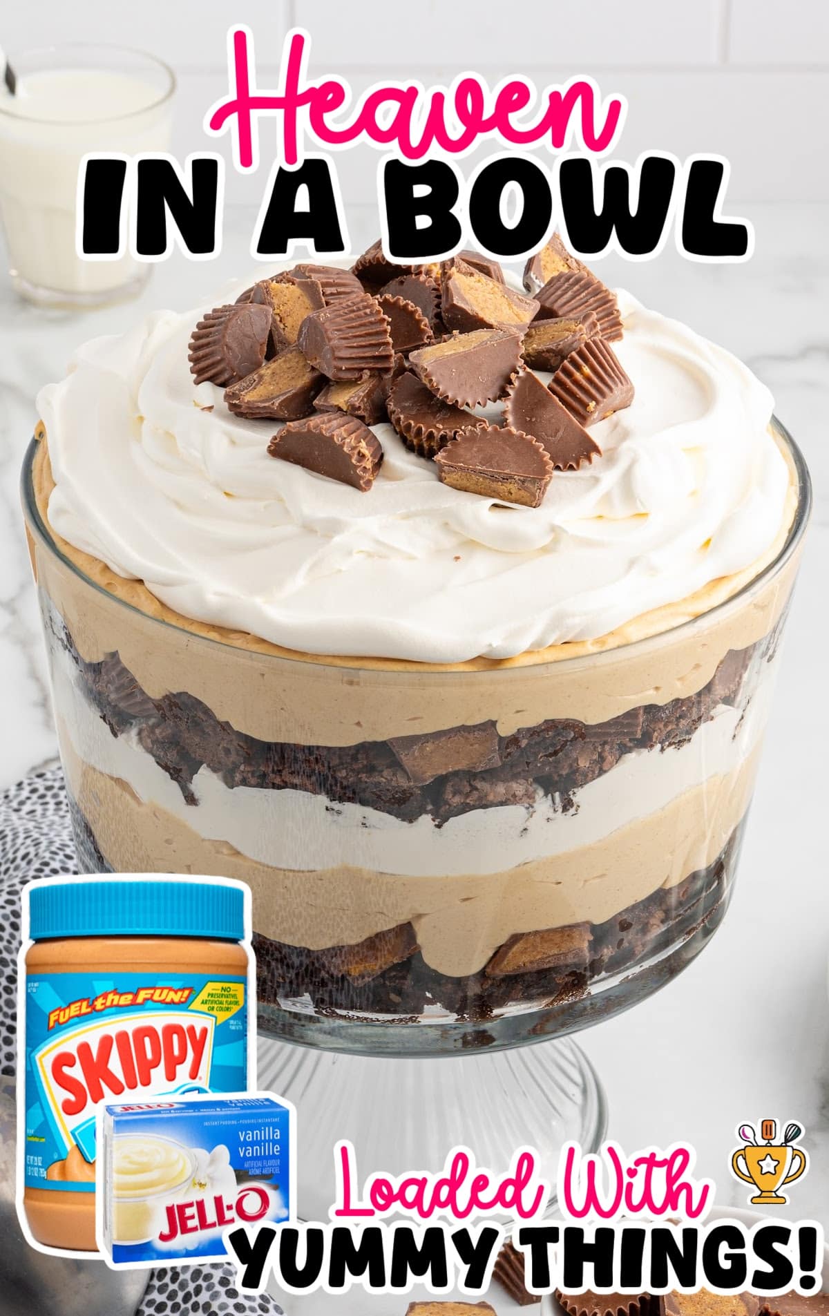 Glass trifle bowl filled with dessert layers of peanut butter mousse, brownies, whipped topping, and peanut butter cups, topped with extra candies.