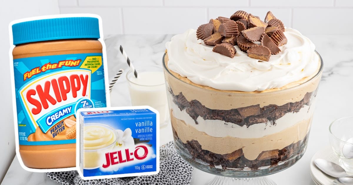 Glass trifle bowl filled with layers of brownies, peanut butter mousse, whipped topping, and chopped peanut butter cups with ingredient packaging shown beside it.