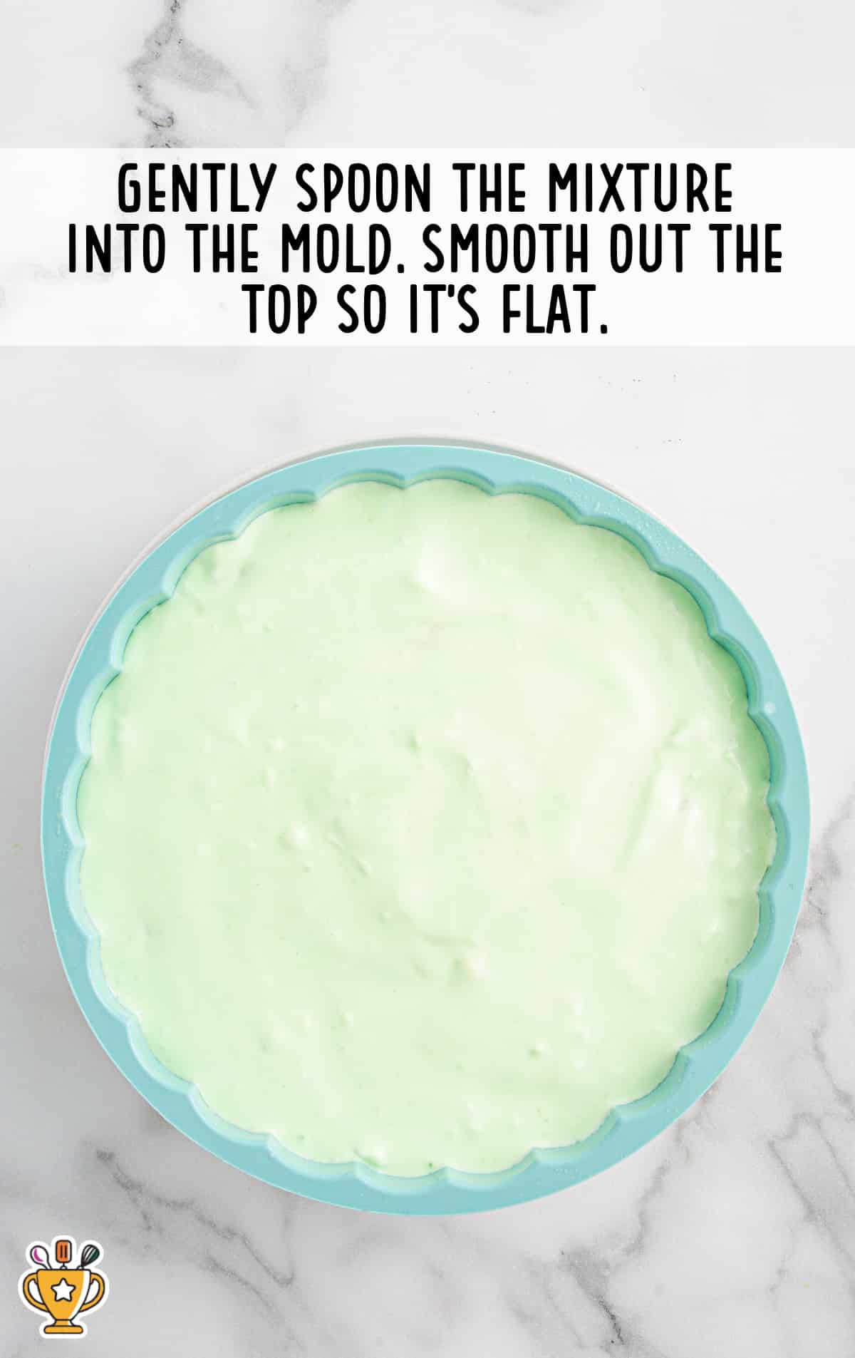The green seafoam mixture spread into a scalloped mold with a smooth, level surface, ready to chill and set.