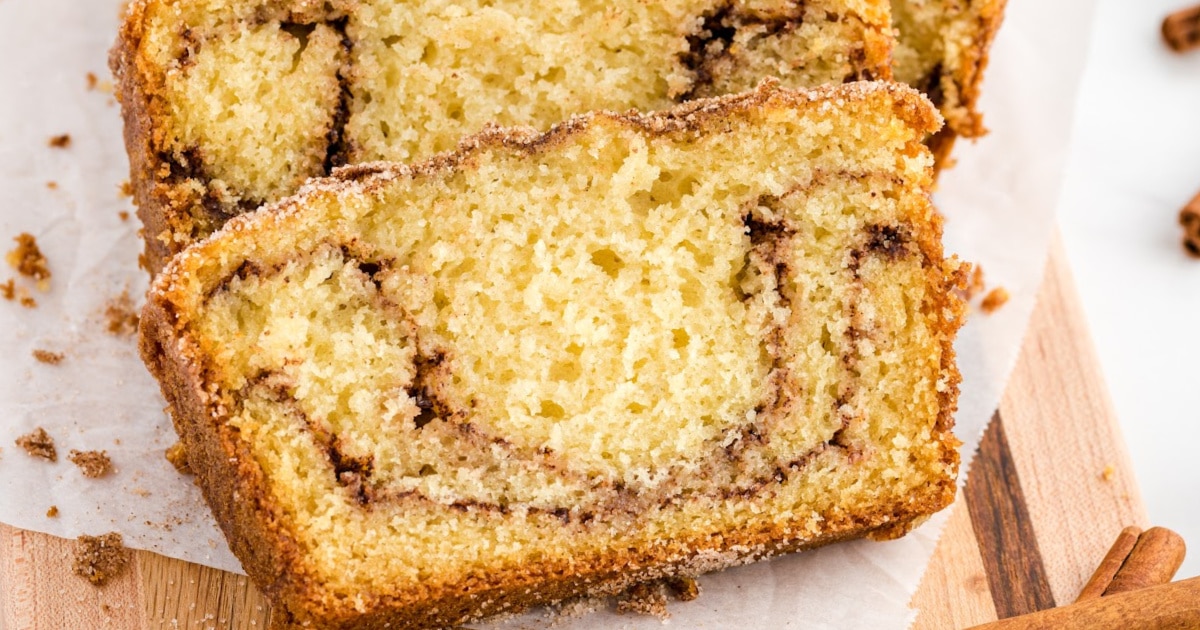 Close-up of two thick slices of golden-brown Snickerdoodle Bread on parchment paper, showing a soft, fluffy crumb with visible cinnamon sugar swirls and a crisp, sugary crust.