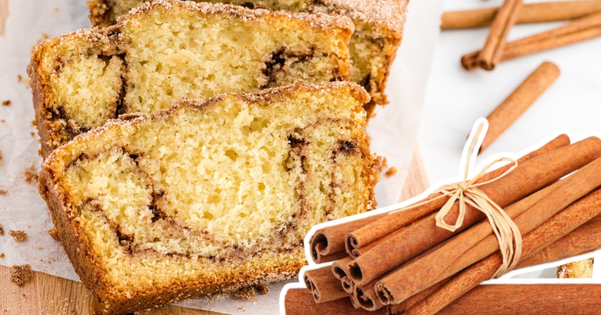 Slices of Snickerdoodle Bread with a cinnamon sugar swirl sit on parchment paper, with a bundle of cinnamon sticks in the foreground for a cozy, spiced touch.