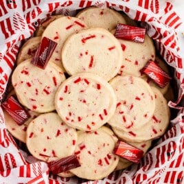Overhead view of peppermint shortbread cookies in a holiday tin lined with red-and-white printed paper, surrounded by Andes peppermint crunch candies.