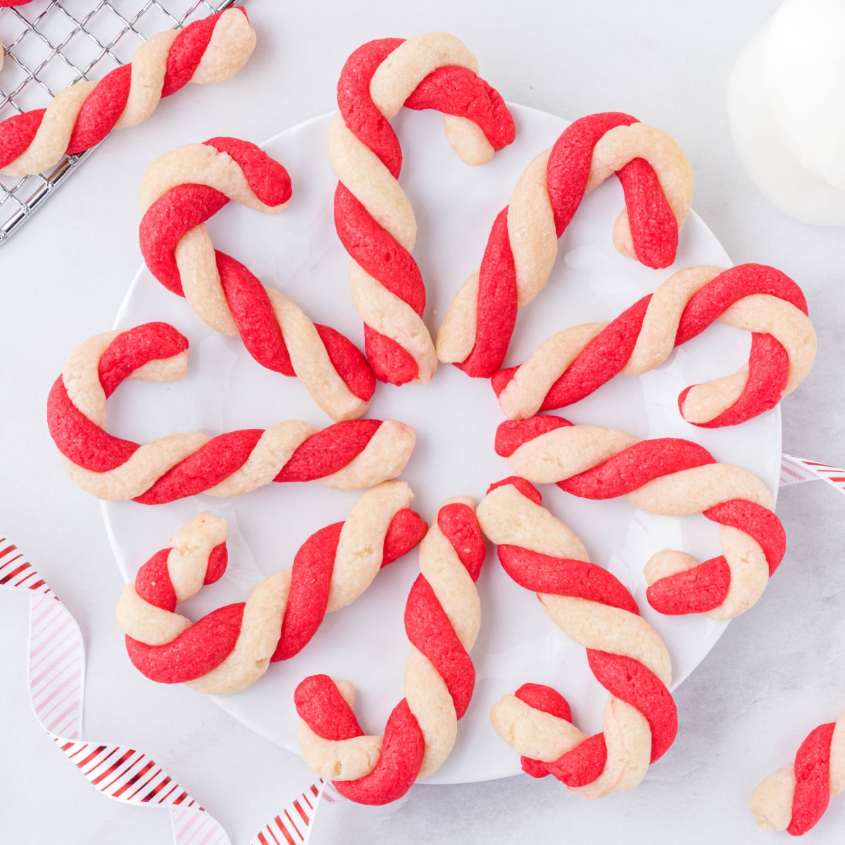 Plate of homemade candy cane cookies twisted with red and white dough, arranged in a circle on a white plate with festive ribbon accents. Easy candy cane dessert.