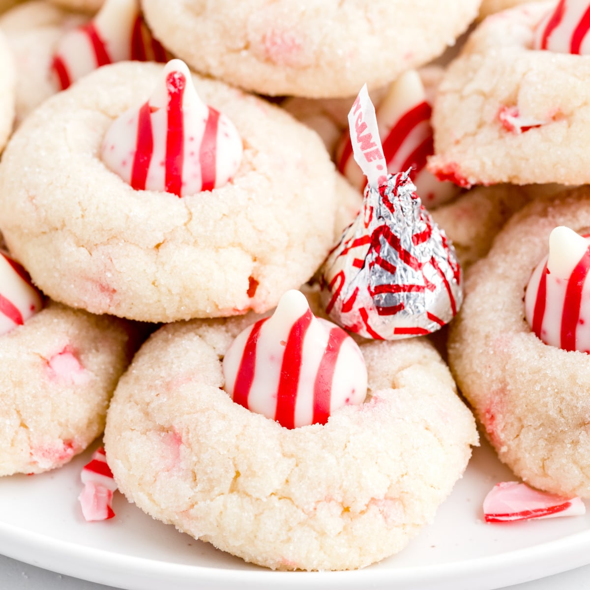 Close-up of candy cane kiss cookies with soft sugar cookie dough, crushed peppermint pieces, and striped red and white Hershey&rsquo;s Candy Cane Kisses on top.