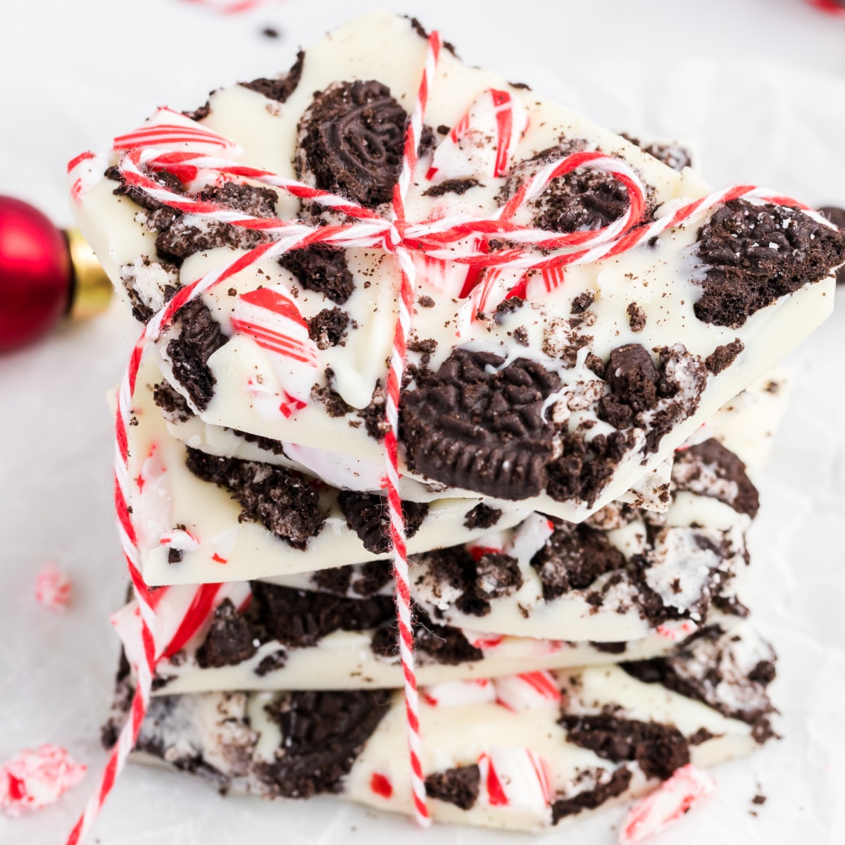 Stack of Oreo peppermint bark with white chocolate layers, crushed Oreo cookies, and candy cane pieces, tied with red and white string for a festive holiday treat.