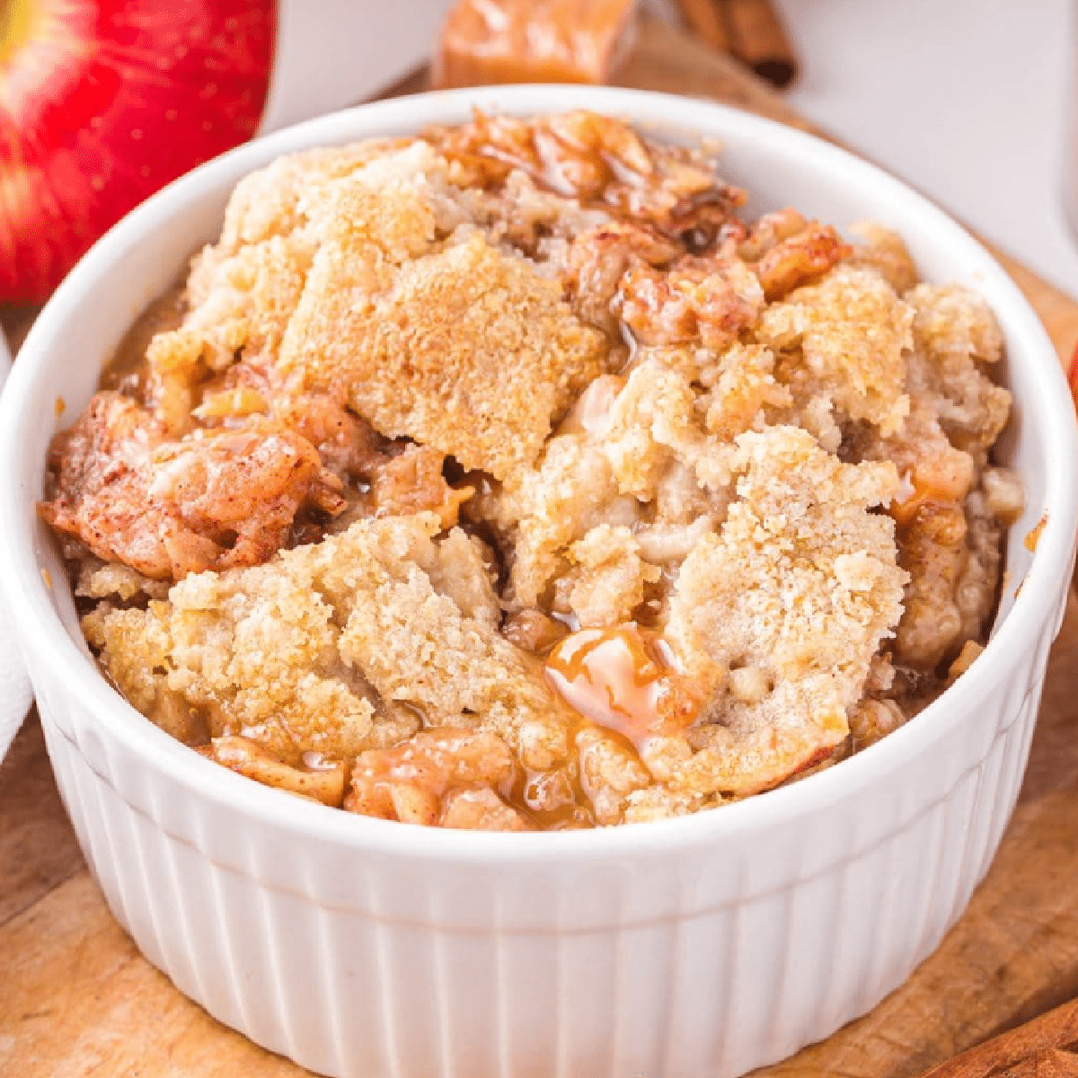Warm and gooey air fryer caramel apple dump cake served in a white ramekin, filled with spiced apple pie filling, golden cake mix topping, and swirls of melted caramel — easy fall dessert made in the air fryer.