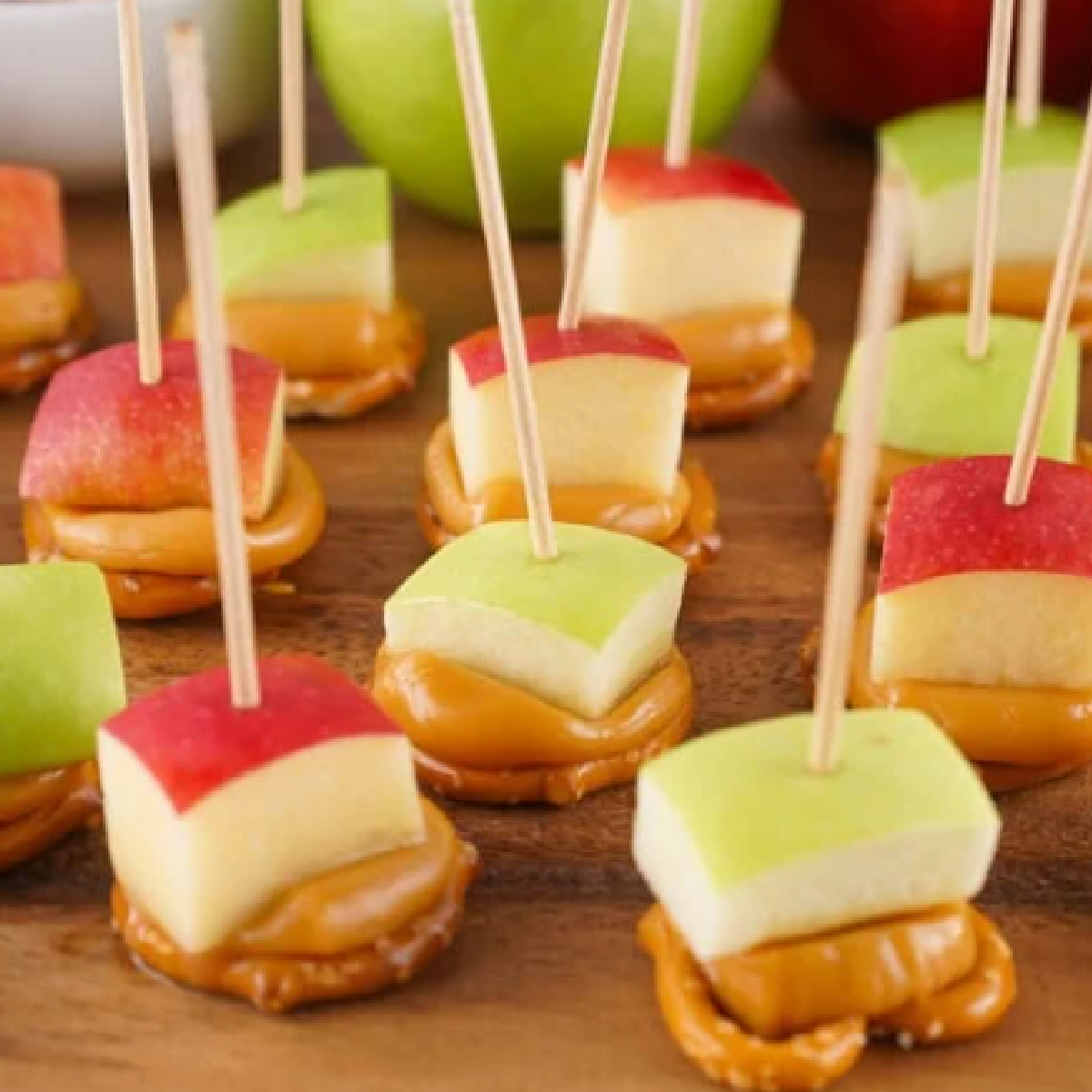Bite-sized caramel apple treats made with red and green apple chunks stacked on soft caramel and mini pretzels, secured with toothpicks — fun and easy no-bake snack perfect for fall parties and after-school treats.