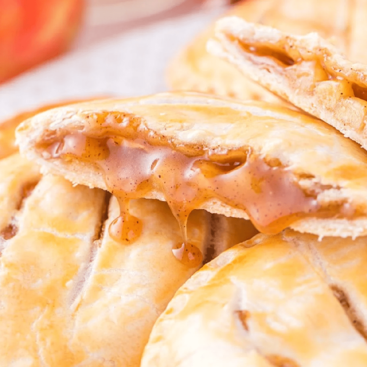 Flaky caramel apple hand pie broken in half to reveal a warm, gooey cinnamon apple and caramel filling, surrounded by golden pastry crust — handheld dessert perfect for fall snacking or lunchbox treats.