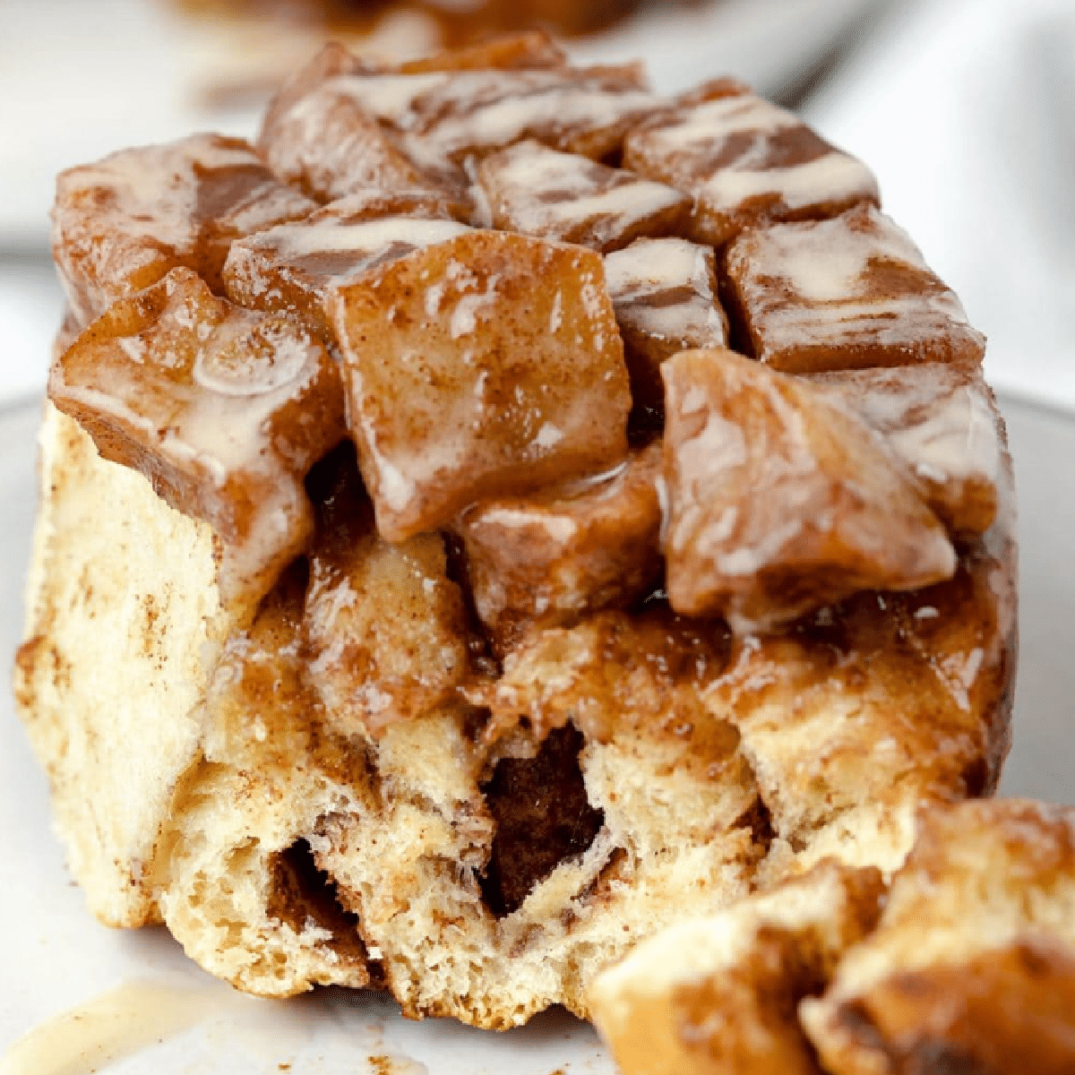 Close-up of a gooey apple pie cinnamon roll topped with soft, spiced apple chunks and a drizzle of creamy glaze.
