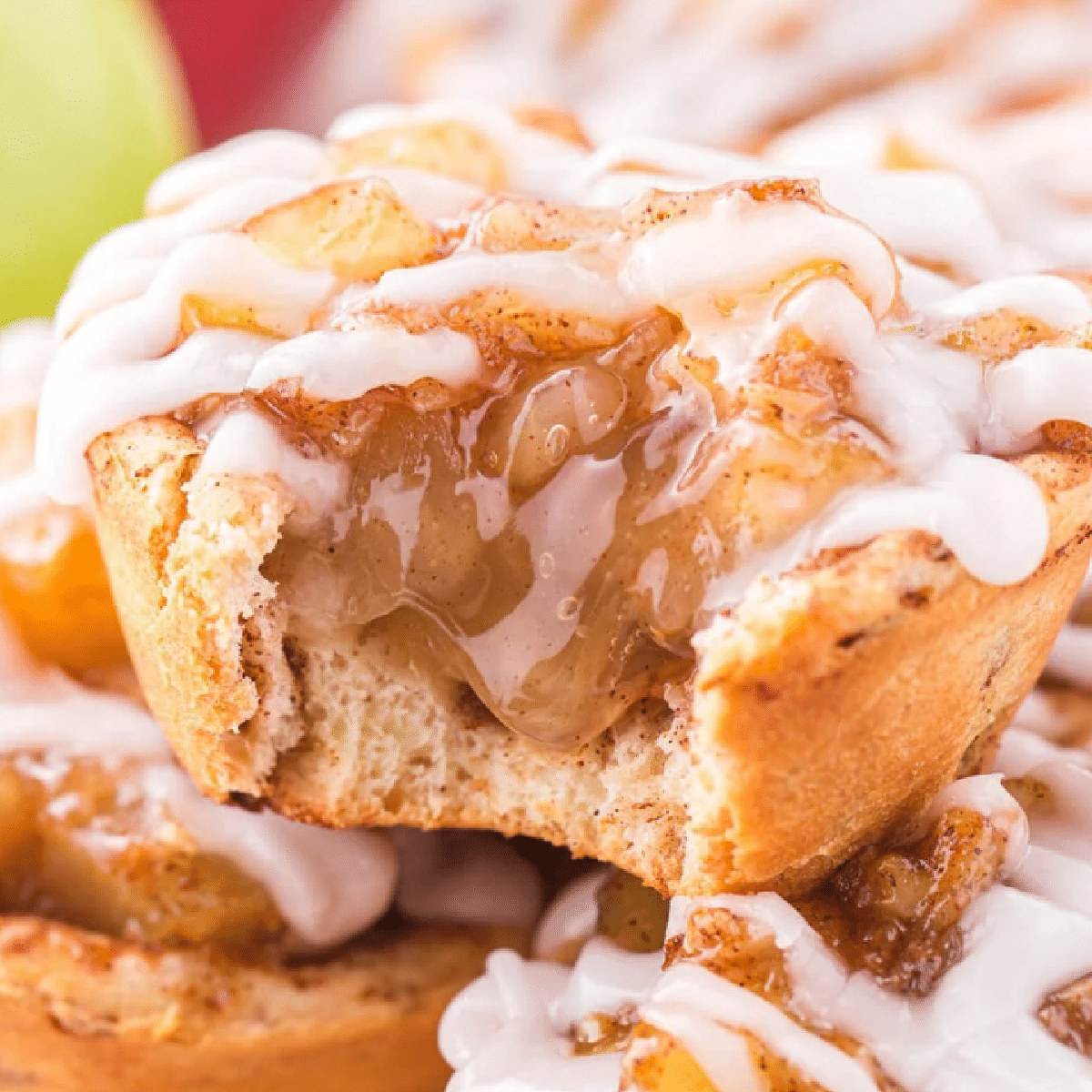 Close-up of a cinnamon roll apple pie cup with a gooey apple pie filling inside a golden-brown cinnamon roll crust, topped with white icing drizzle — handheld fall dessert made in muffin tins for easy serving.