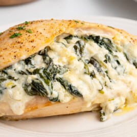 Juicy baked chicken breast stuffed with creamy spinach and melted cheese, served on a white plate with herbs.