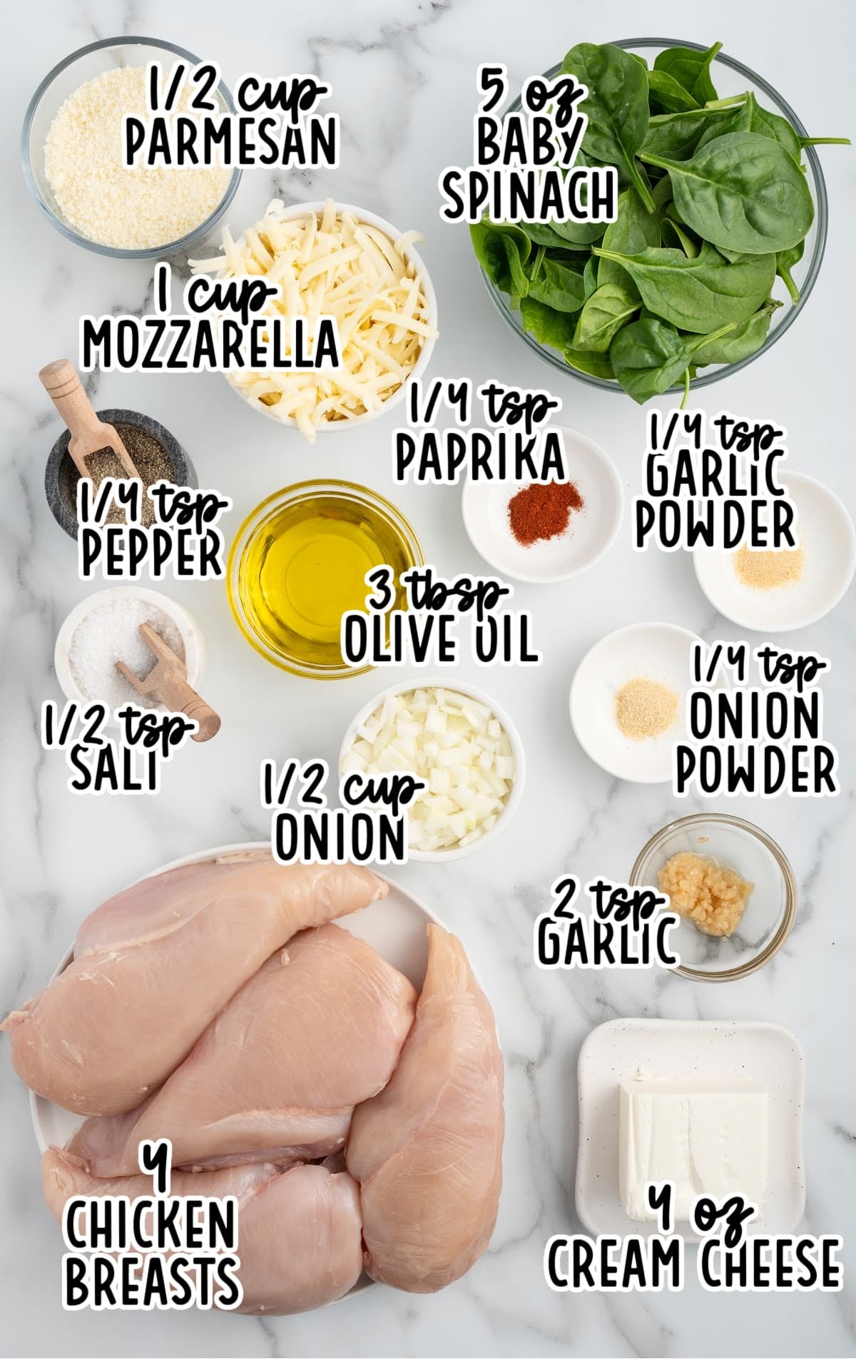 Flat lay of ingredients for spinach stuffed chicken breast, including raw chicken, spinach, cheeses, onion, garlic, spices, and olive oil labeled for easy prep.