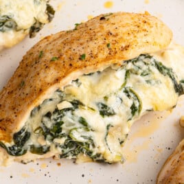 Alt text: Close-up of a baked spinach stuffed chicken breast with a golden seasoned exterior and creamy spinach and cheese filling oozing out onto the plate.